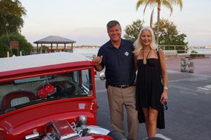 Couple posing by a red vintage car with Gulfport waterfront at sunset