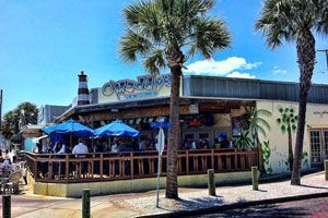 O'Maddy's exterior with palm trees and blue umbrellas on a sunny day