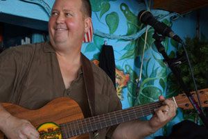 Live musician playing guitar with tropical mural behind him